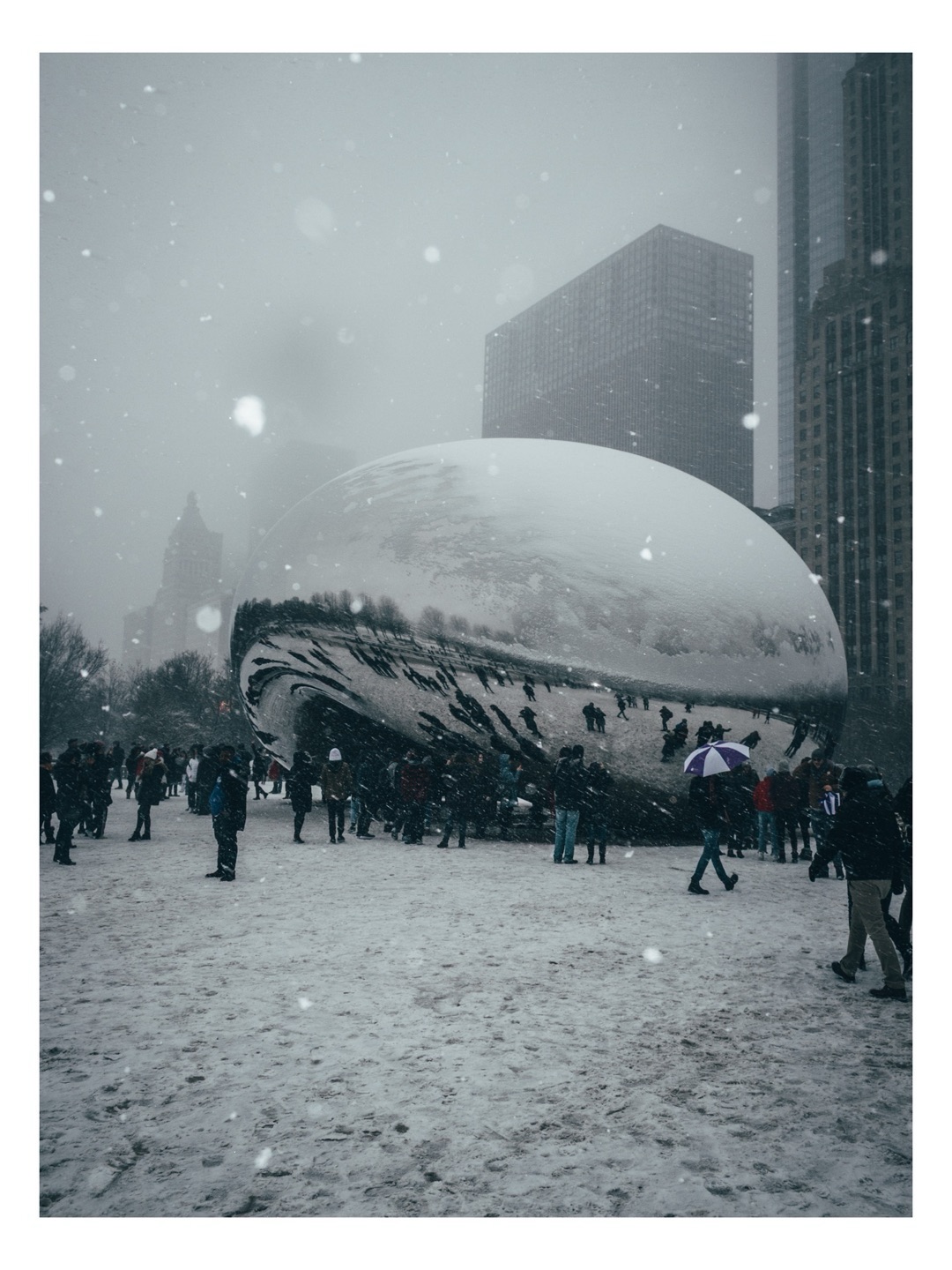 Snow falls around the Bean as visitors cross Millennium Park.