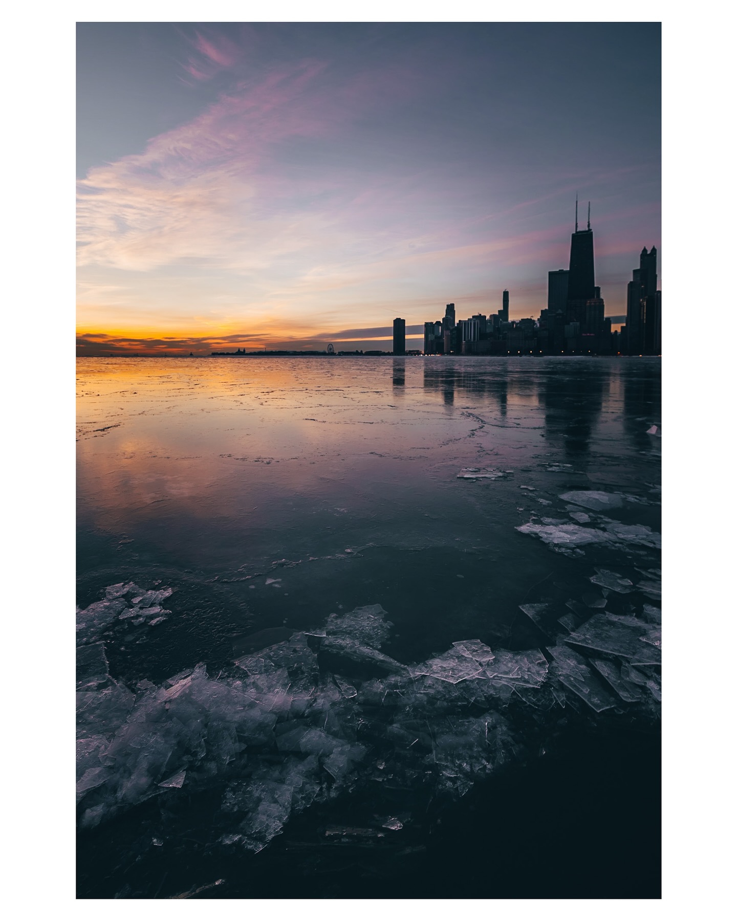 Broken ice and skyline reflections beneath a pink and gold sky.